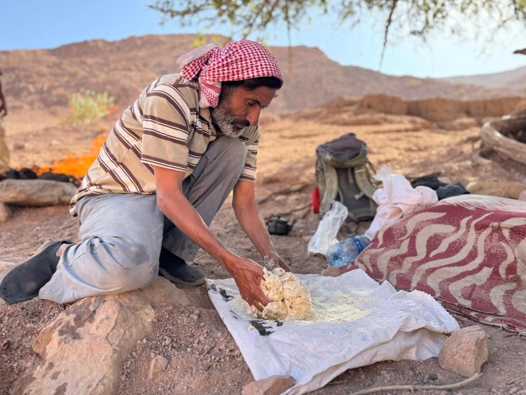 Local guide kneading dough by a campfire in the desert